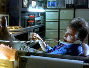 John in his office, on the phone, glass of whiskey in hand