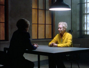 Emma, in bright yellow jacket, being interrogated.