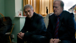 Steve and Gerry, looking concerned as they sit on a sofa