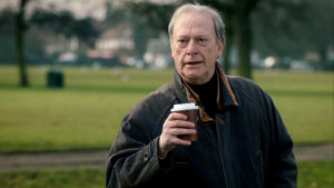 Gerry, outside, looking delighted, coffee cup in hand.