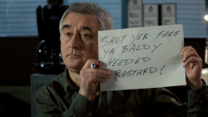 Steve holds up a handwritten message. It reads "Shut yer face ya baldy heeded bastard!"