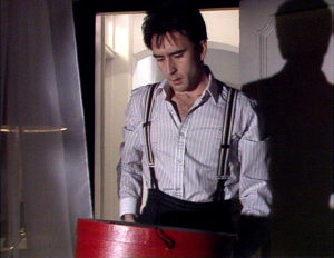 Eddie, half dressed in shirt and suspenders, finds a hatbox